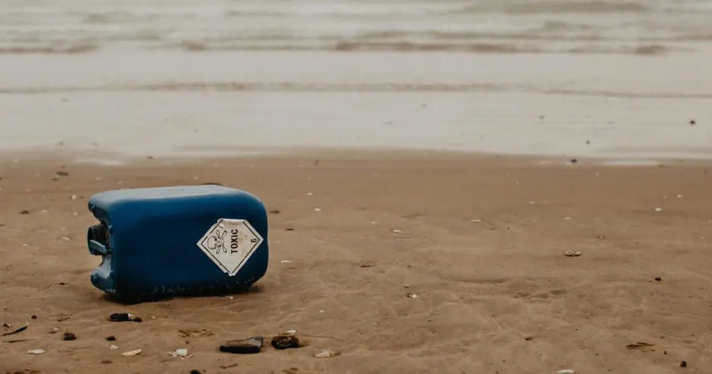 A large blue can lying on the beach reads "Toxic."