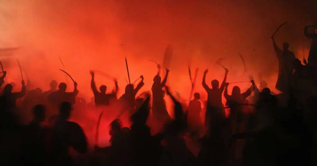 A group of people with hands in the air surrounded by and orange glow. It looks violent