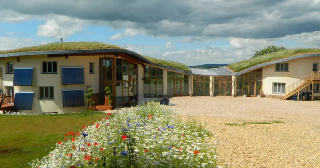 A sprawling 2-story yellow cob home with solar panels and a grass roofs.