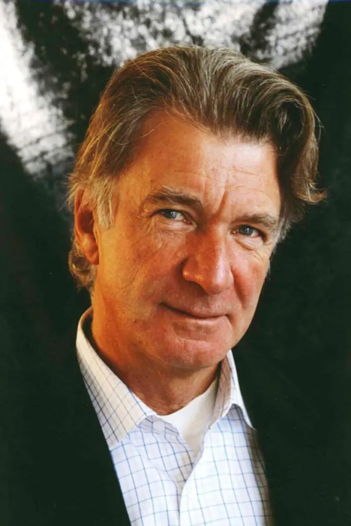 A man with gray hair, Anders Wijkman is wearing a dark jacket and a white checkered shirt, posing against a dark, textured background.