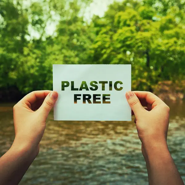 A plastic free sign help up in front of a river and trees