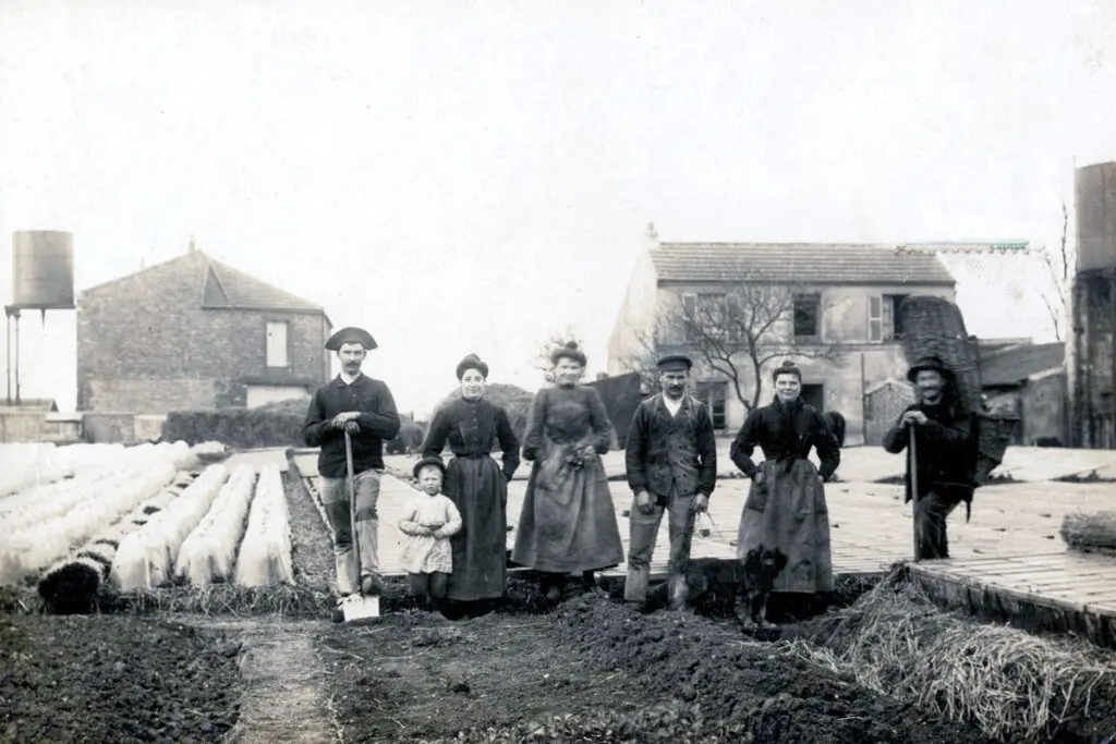 Old black and white photograph of farmers in the field with a toddler and a dog.