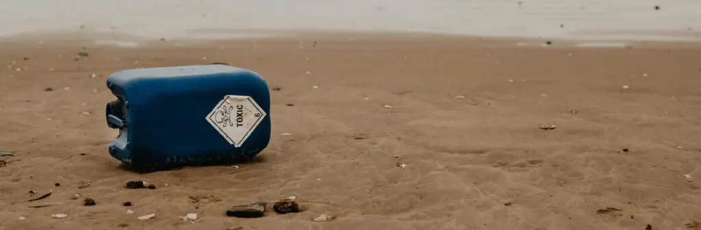 A large blue can lying on the beach reads "Toxic."