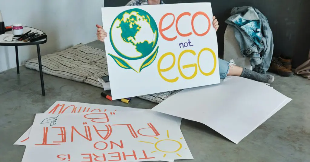 A person is holding a sign with the message "Eco not Ego" accompanied by a hand-drawn globe design. They sit on the floor, encircled by additional protest signs including one that declares "There is no Planet B," stressing the critical nature of Climate Change. Beside them lies a jean jacket. This scene seems to reflect sentiments similar to those discussed in the Social_Excerpt_What-does-climate-hypocrite-mean post.