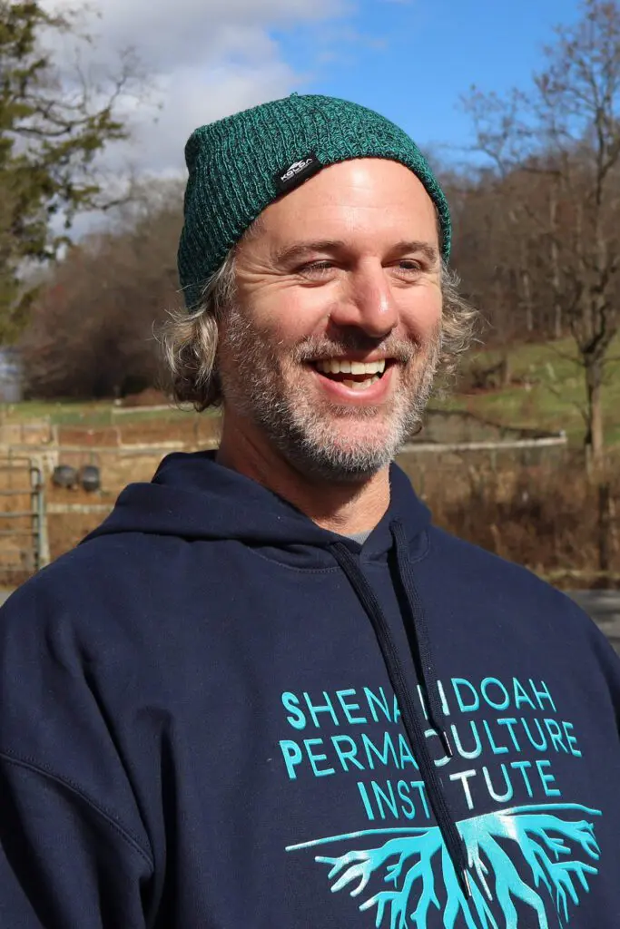 Ryan Blosser, in a green beanie and blue hoodie, smiles outdoors on a bright day.