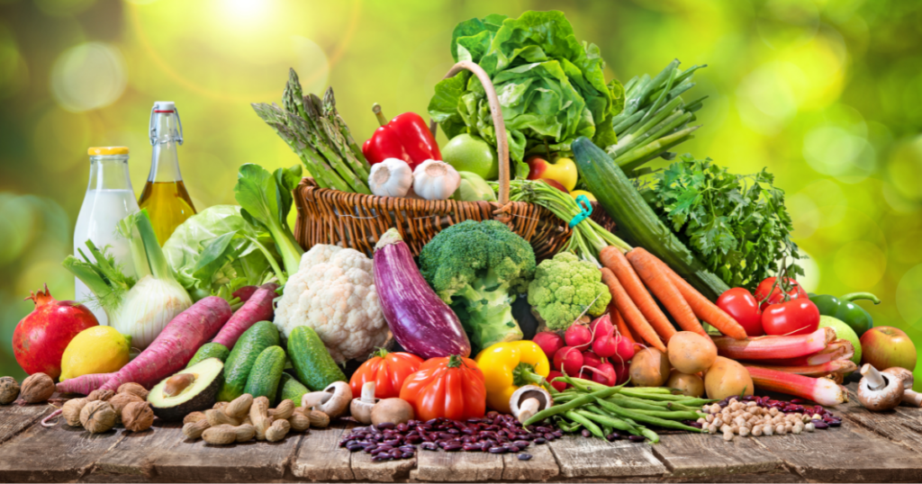 A vibrant array of organic food, featuring fresh vegetables and fruits, beautifully arranged on a wooden table outdoors.