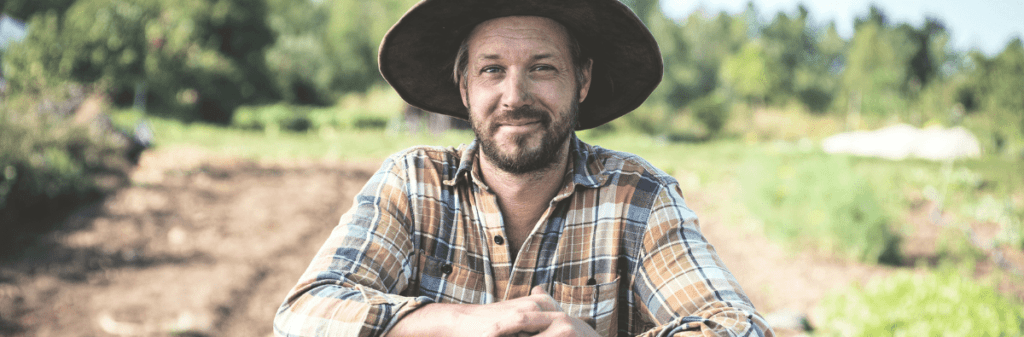 A man in a plaid shirt and hat stands in a sunny, rural setting, embodying essential lessons of farm life.