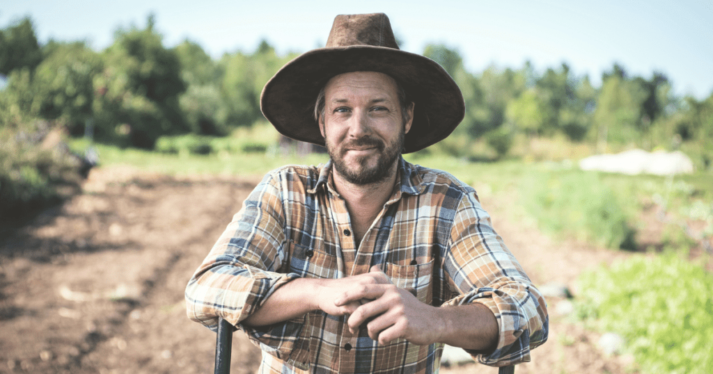 A man in a plaid shirt and wide-brimmed hat stands in a field, embodying essential lessons of farm management.