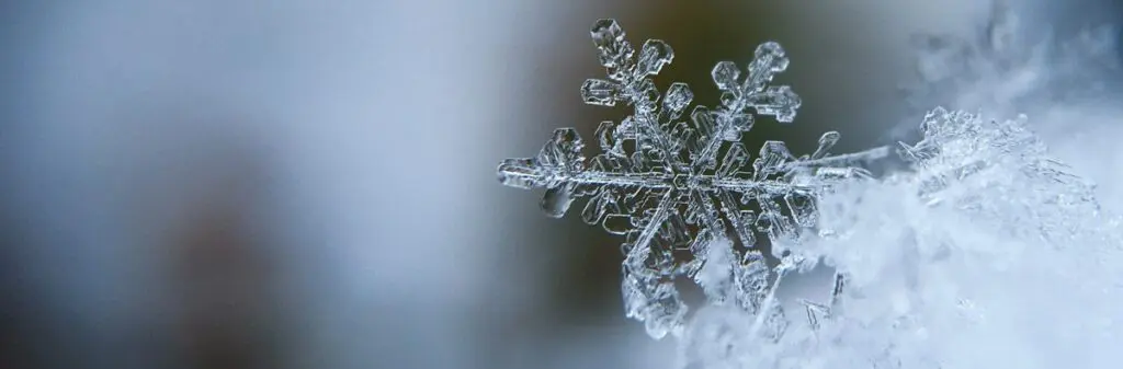 Close-up of a single snowflake with intricate details, capturing the beauty of frozen light against a blurred icy background.