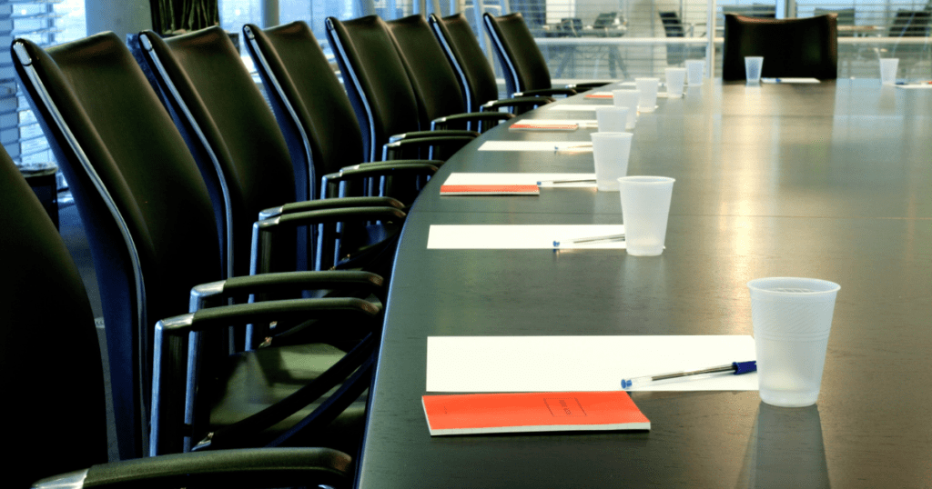 The empty boardroom, ready for an interview, features a long table surrounded by chairs with neatly placed notepads, pens, and plastic cups.