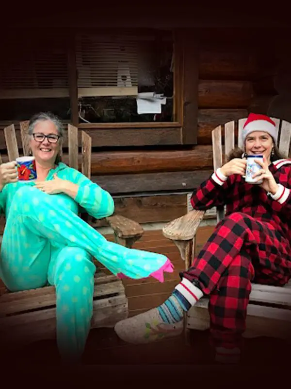 Two people in cozy onesies and slippers sip from mugs on wooden chairs, enjoying a serene moment filled with the warmth of conscious gifting.