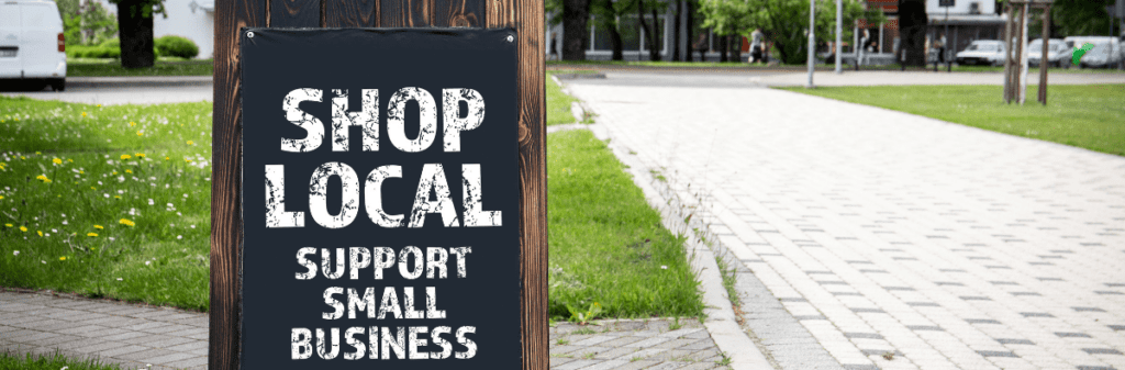 A sign on a wooden post by the path reads, "Shop Local Support Small Business," reminding passersby of the importance to support local shops.