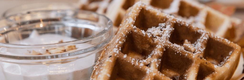 Close-up of zucchini waffles dusted with powdered sugar, next to a bowl of creamy dip. Savor the delightful twist on a classic treat that’s perfect for any holiday brunch.