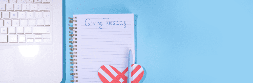 A laptop, notebook with "Giving Tuesday," pencil, and heart decoration rest on a blue background, embodying the spirit of giving back. It's the perfect setup to jot down ideas inspired by New Society Publishers and their commitment to positive change.