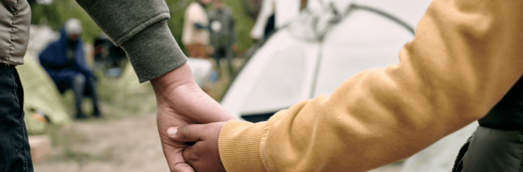 Two people holding hands, embodying true connection at a lively campsite.