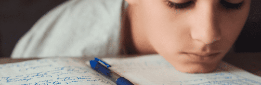 Person resting head on desk near a notebook and pen, dreaming of a globally connected world.