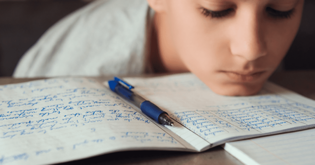 Person resting head on desk with open notebook and pen, lost in schooling thoughts.