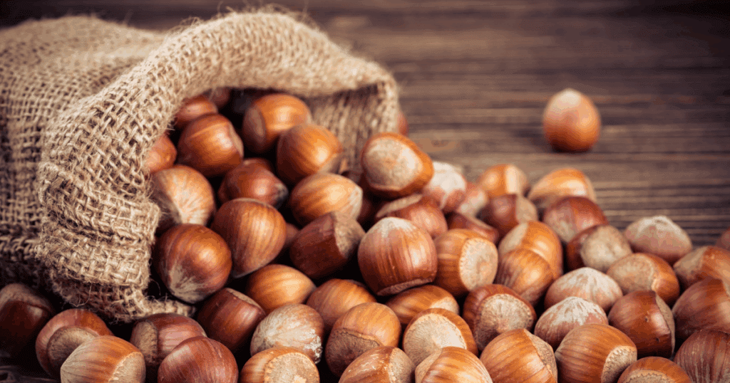 A burlap sack spills hazelnuts—a nutty idea—onto a rustic wooden surface.