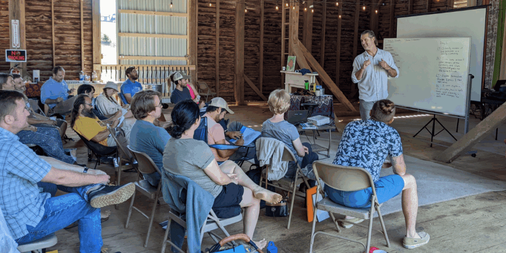 A group maps their inner landscape and build relationships as Ryan Blosser presents by a whiteboard in a rustic setting.