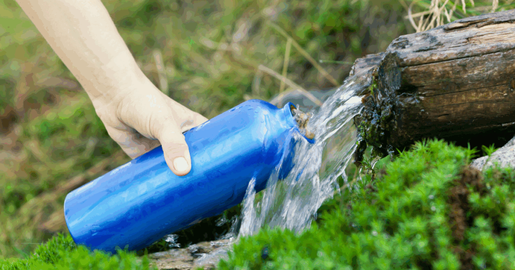 Reusable containers are perfect for outdoors. Hand filling a blue water bottle from a natural stream in the outdoors during summer.