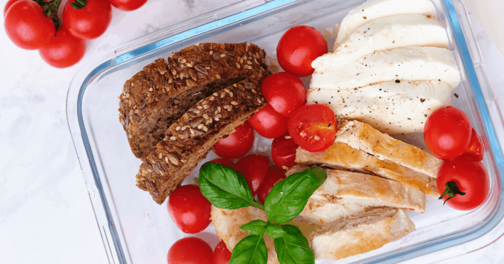 Reusable containers are perfect for outdoors: glass container with sliced bread, tomatoes, mozzarella, and grilled chicken.