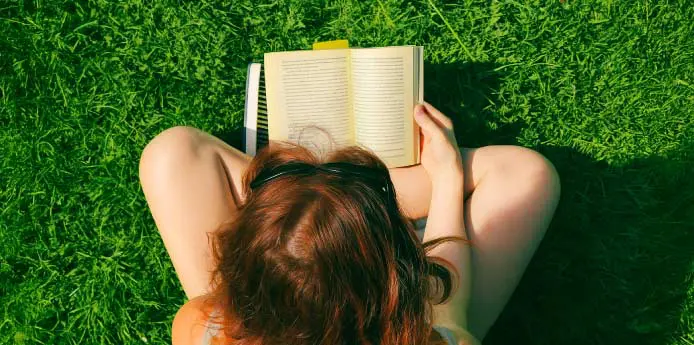 Person sitting on grass and reading a book, viewed from above.