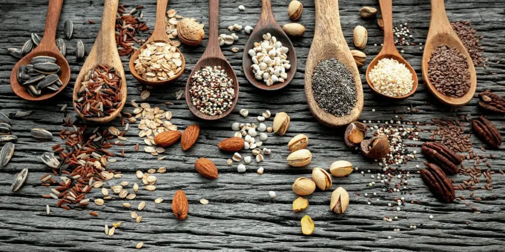 Wooden spoons with various grains, seeds, and nuts on a rustic wooden surface.