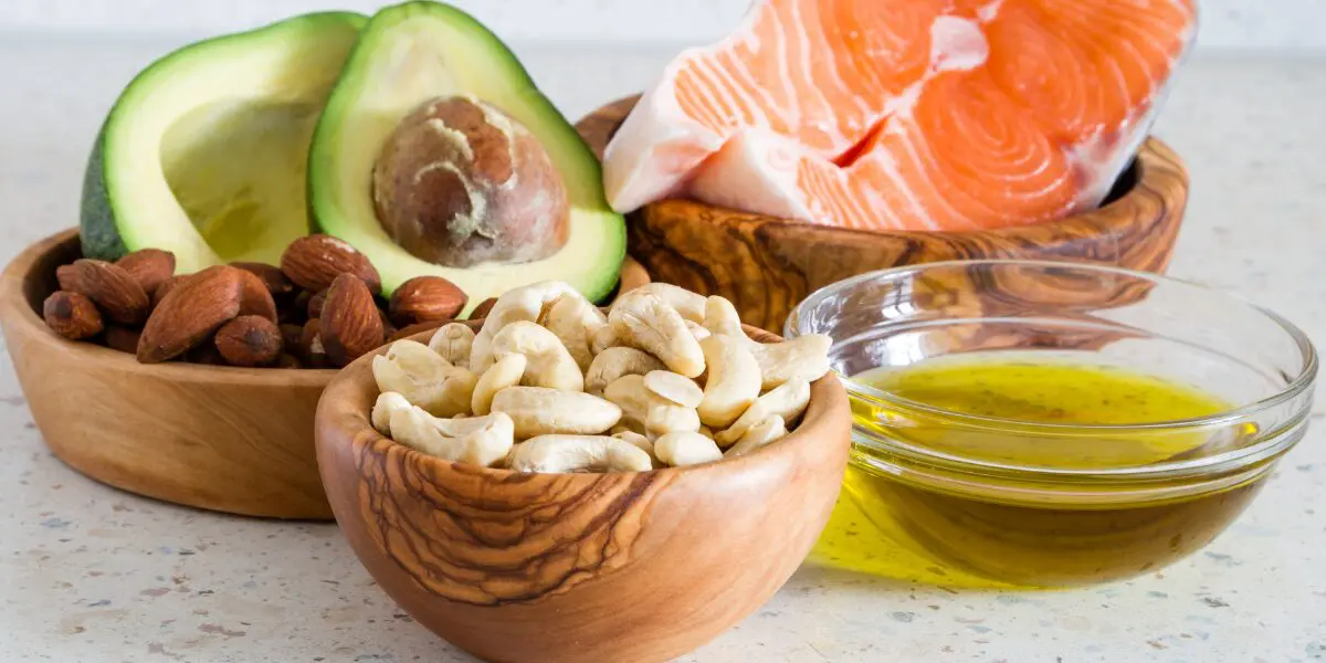 Bowls of nuts, avocado halves, salmon steak, and grains on a kitchen counter.