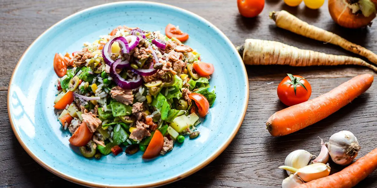 Low fat meal of salad with tuna, onions, veggies, and nuts surrounded by fresh produce.