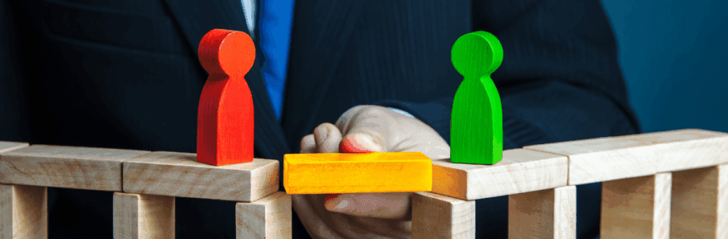 A hand uses mediation to connect red and green figures with a yellow block on a wooden bridge.