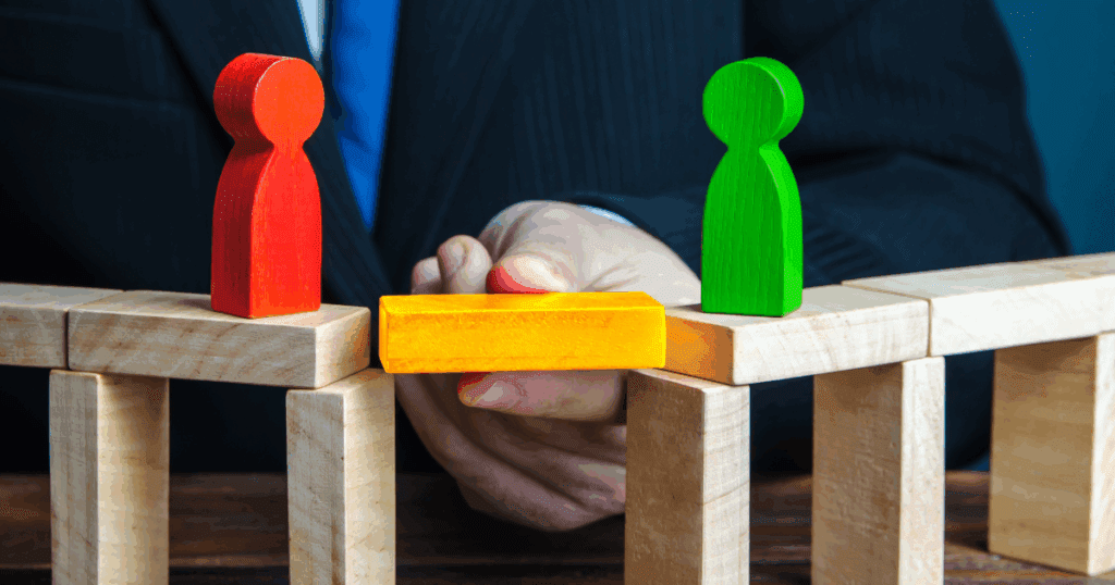 A hand connects two wooden figures with a yellow block, symbolizing mediation and agreement.