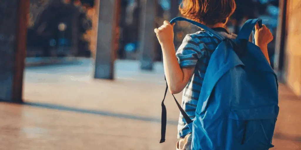 Back to school, child wearing a blue backpack outdoors, radiating summer joy on a sunny day.