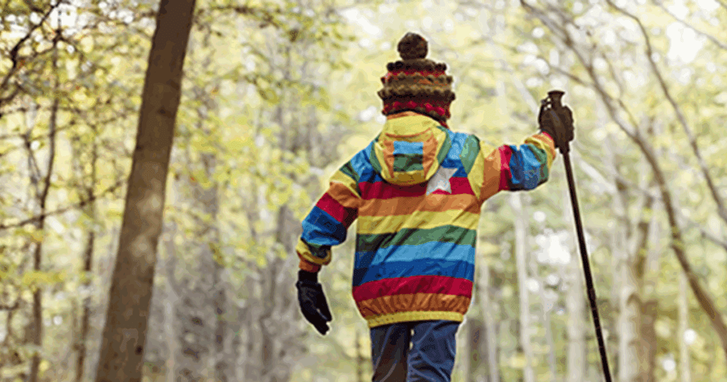 Child hikes in a forest, enjoying outdoor play with a walking stick.