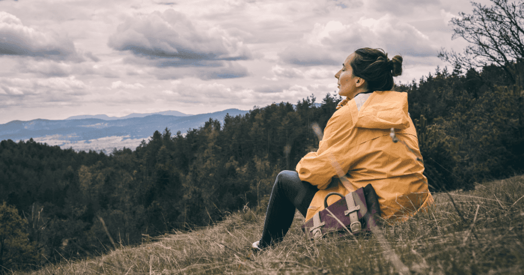 Person in yellow jacket sits on grassy hill, gaining a better sense of nature and calm.