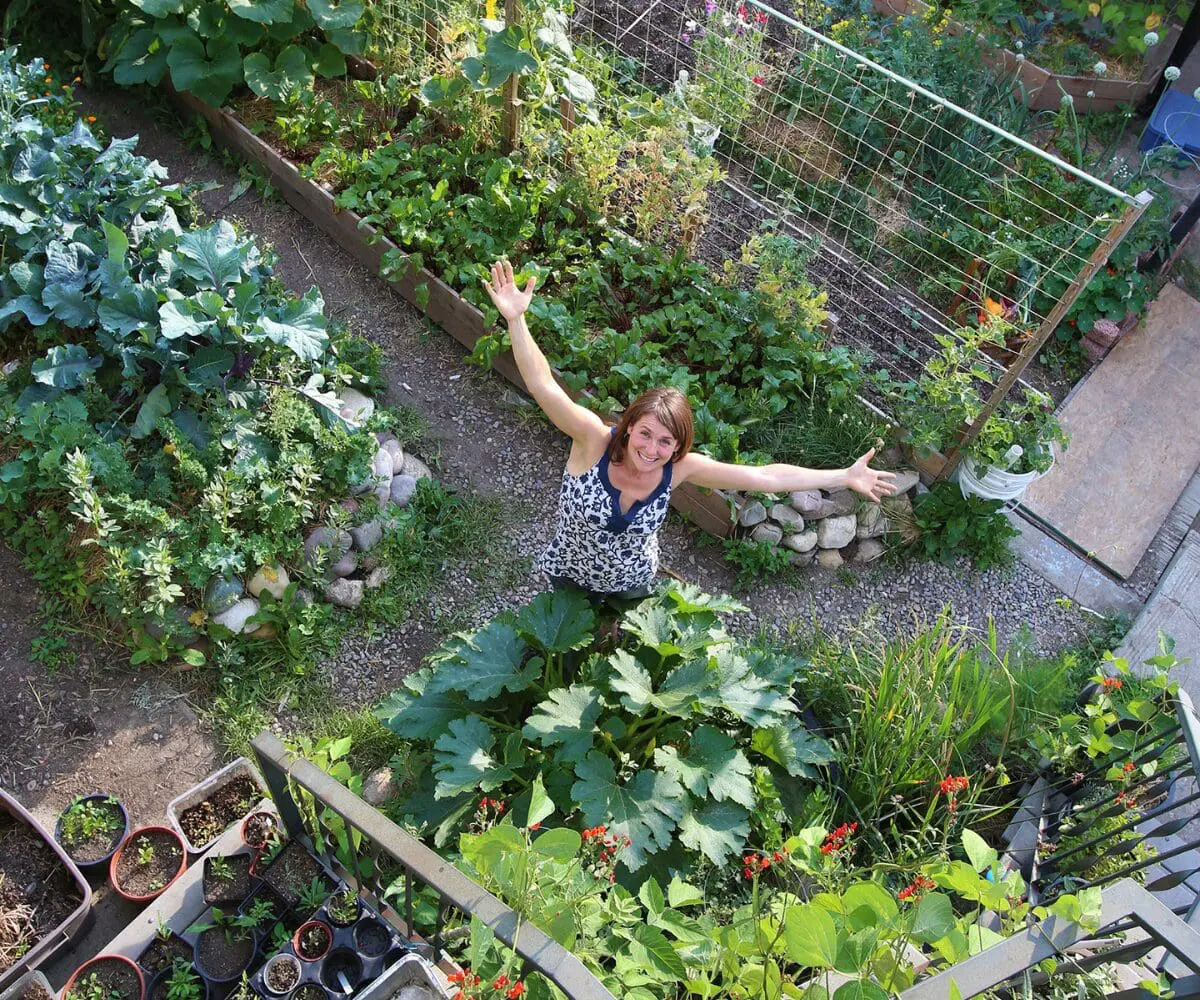 Woman standing in a lush vegetable garden, celebrating rainwater harvesting from above.