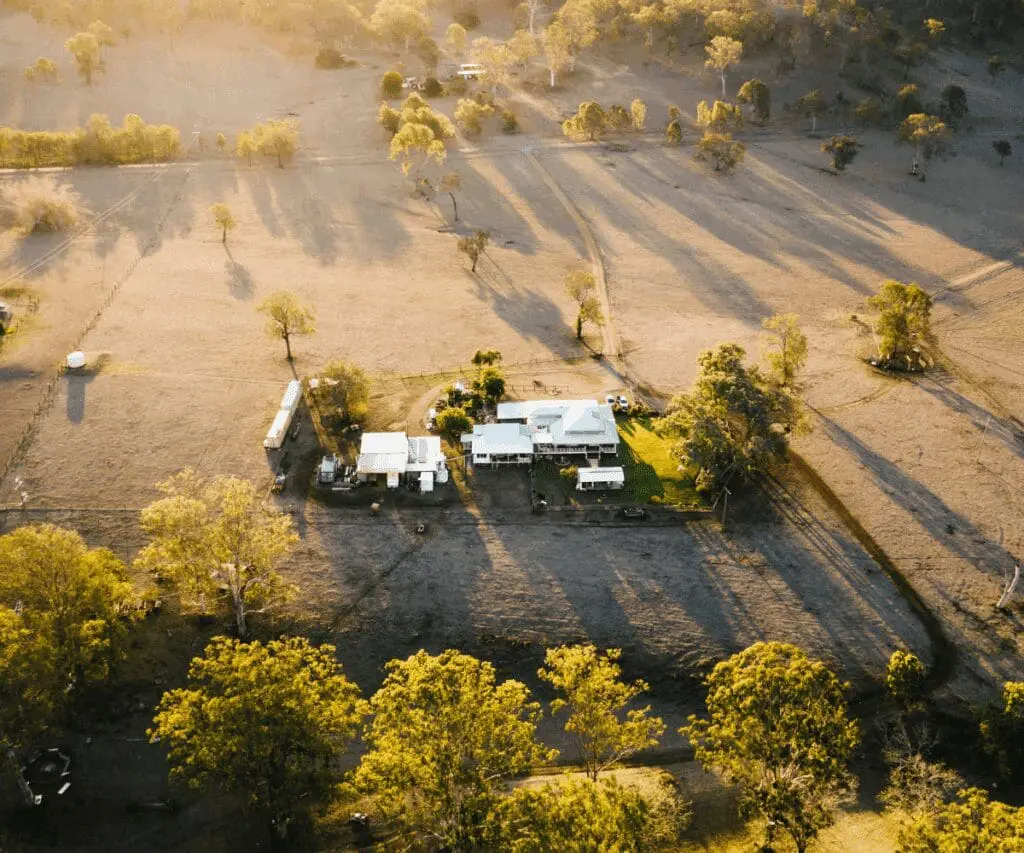 Aerial view of a farmhouse with rainwater harvesting, surrounded by dry fields at sunset.