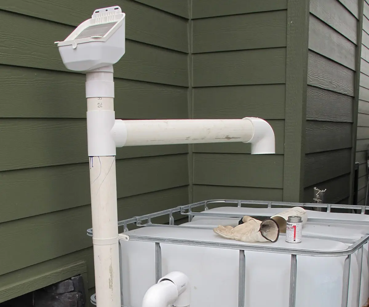 Rainwater harvesting PVC pipe system enhances water security by the green wooden wall and tank.