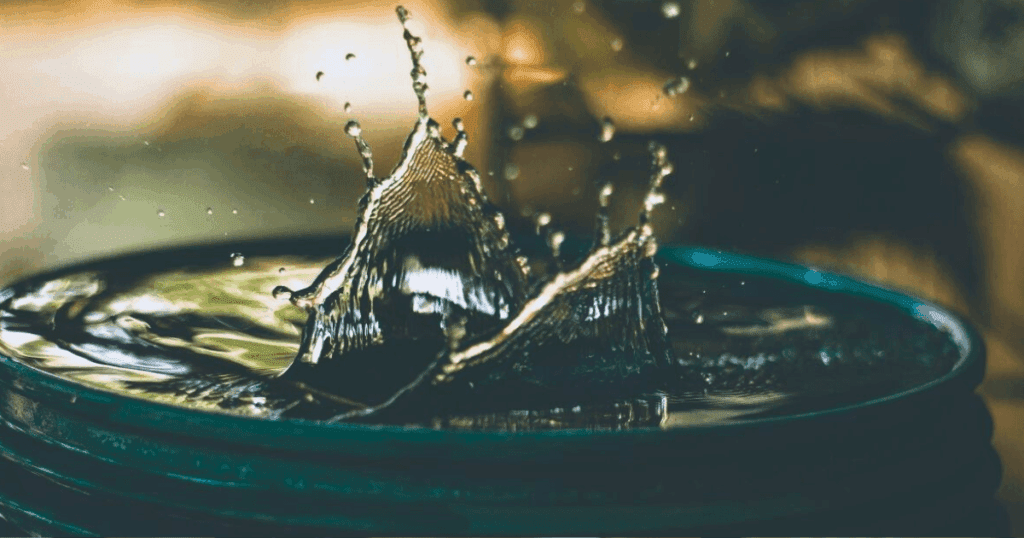 Water splashing in a container, capturing sharp droplets and motion in soft natural light.
