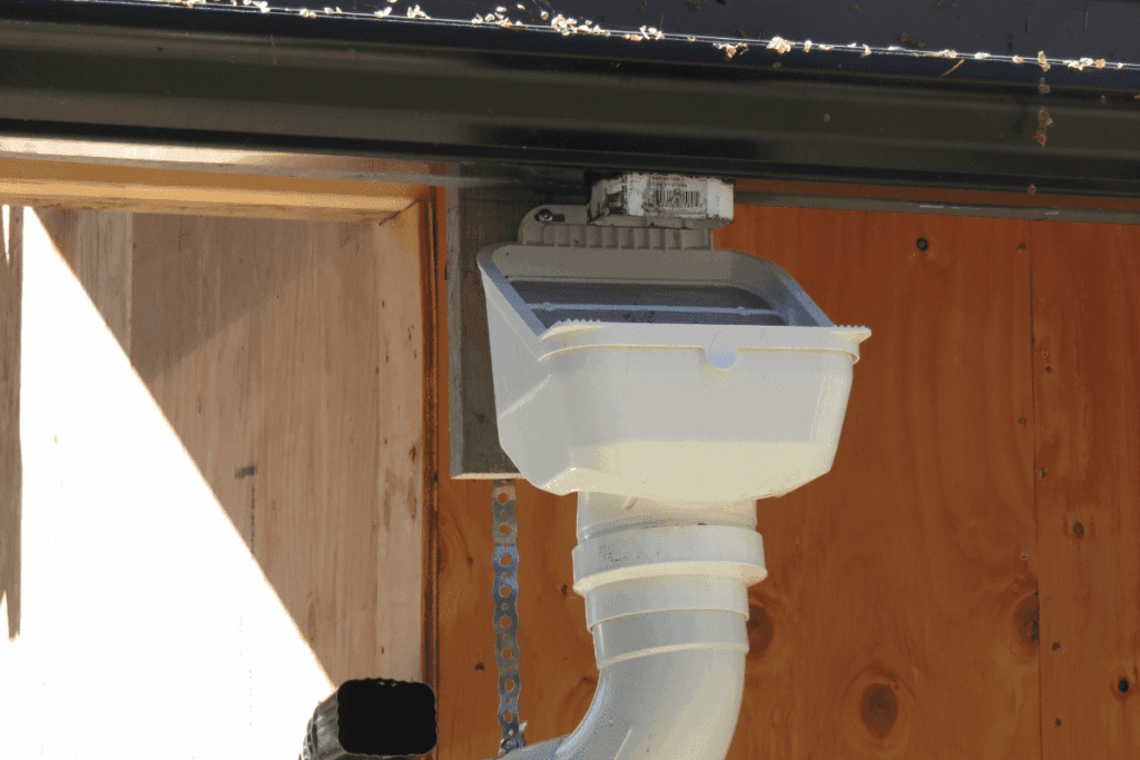White rain gutter filter box attached to a wall with a curved drainpipe below it.