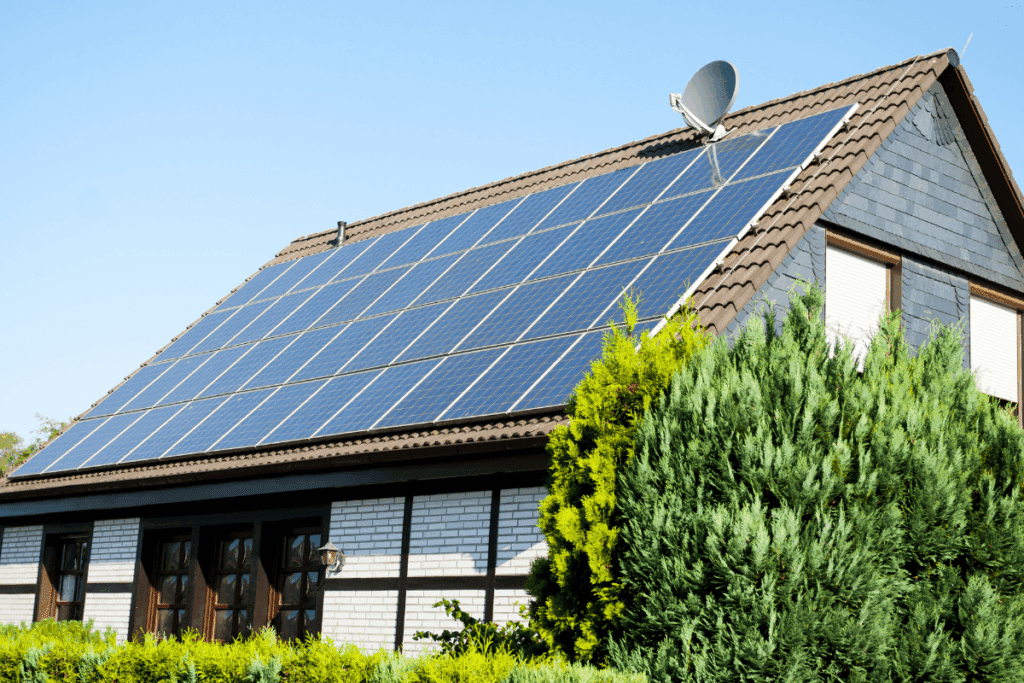 House with solar panels using 100% Clean Power, surrounded by green bushes under a blue sky.