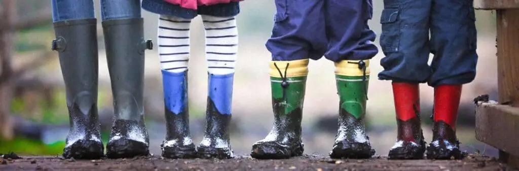 Four children in colorful rain boots explore muddy ground—talk to your kids about climate change.