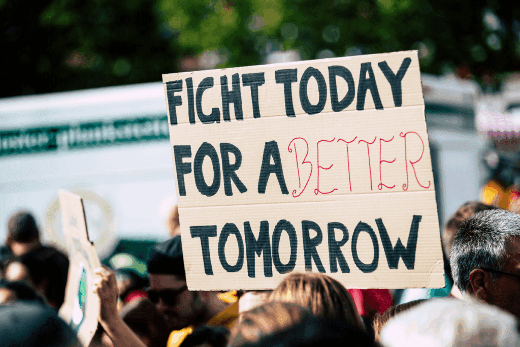 A protest sign on climate change reads "FIGHT TODAY FOR A BETTER TOMORROW" above a crowd.