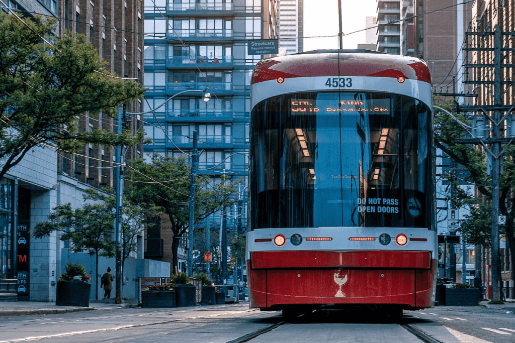 Red streetcar travels through city street, promoting sustainability among tall buildings and trees.