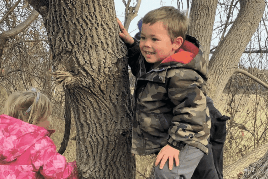 Two children, timeless in their joy, climb and watch, embracing stewardship principles outdoors.