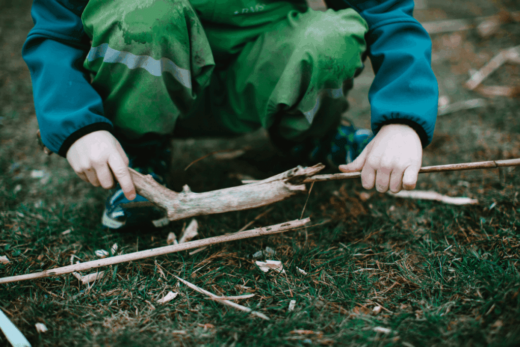 Outdoor play. Child in green gathers sticks in nature.