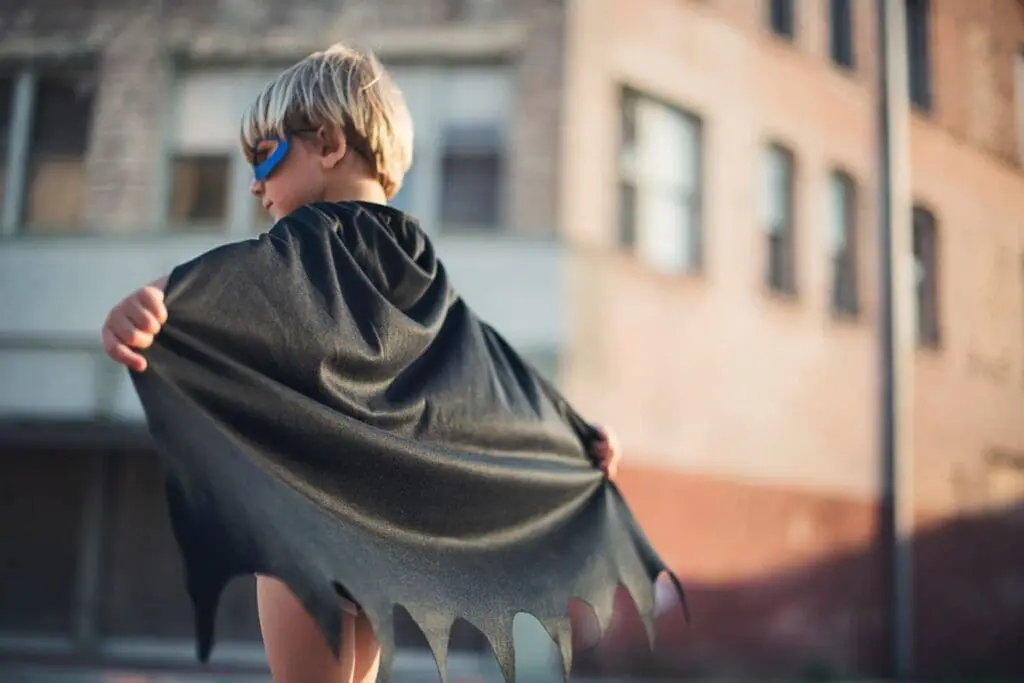 Young child in a black cape and mask poses like a superhero, ready to fight climate change.