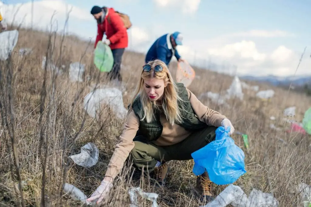 People picking up litter in a grassy field, teaching kids about climate change for 2025.