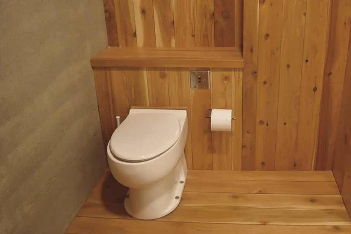 White composting toilet and toilet paper in a wooden-paneled bathroom with a concrete wall.