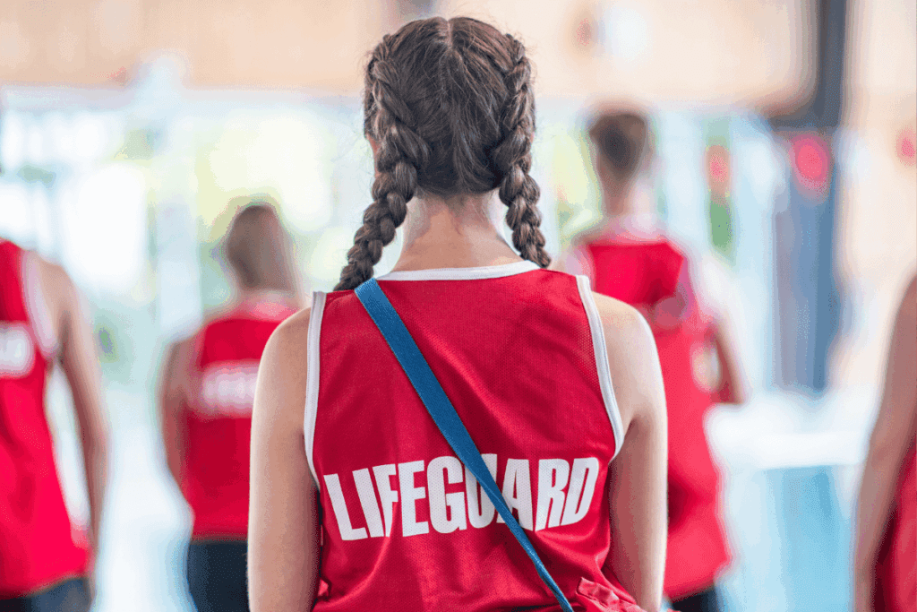 Teenage girl with braids in a red "Lifeguard" shirt, embodying thriving youth, seen from behind indoors.