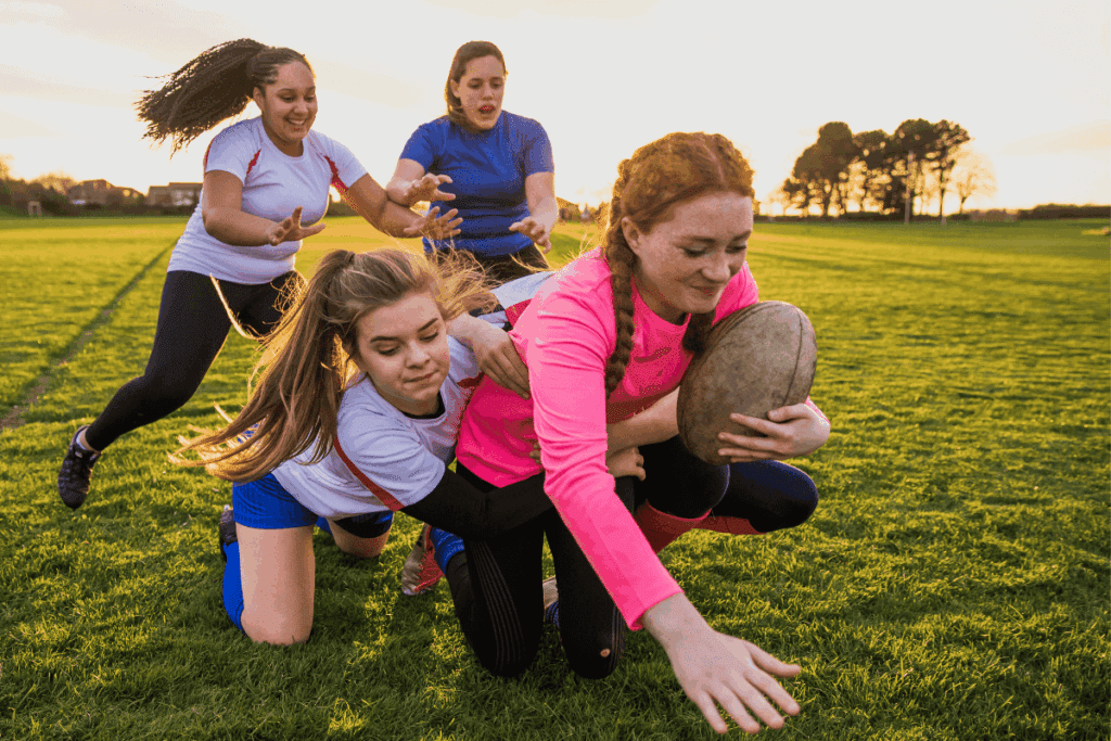 Four girls play rugby at sunset, showing youth leadership as one reaches to score while tackled.